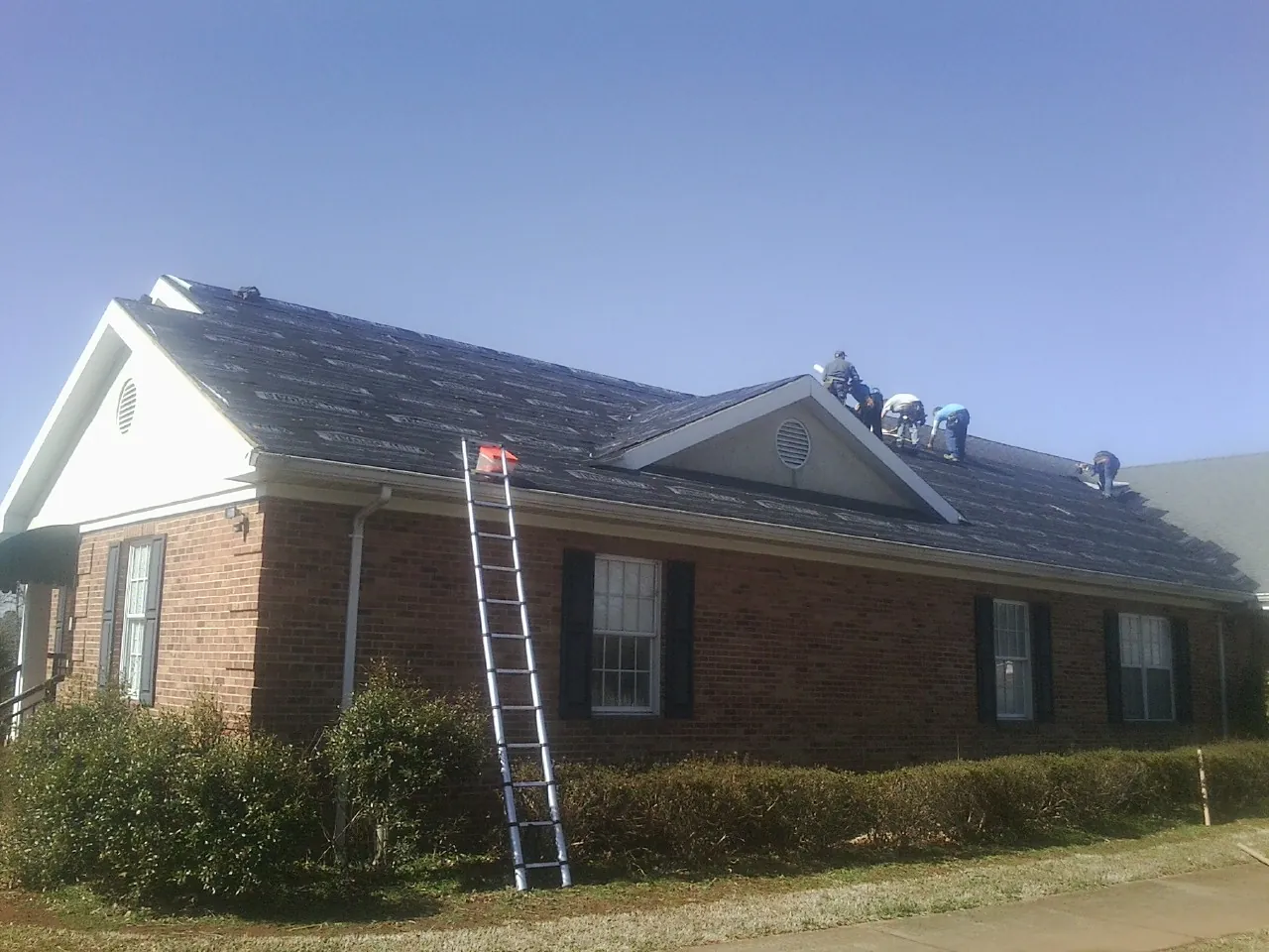 Crew tearing shingles off a brick ranch roof with a ladder set — Metal Roof Repair work by our crew in Cleves