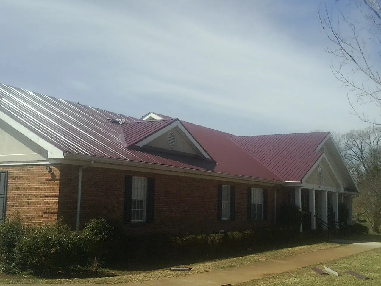 Red metal roof with gabled entries on a long brick building, from a Hail Damage Roof Repair job in Cleves