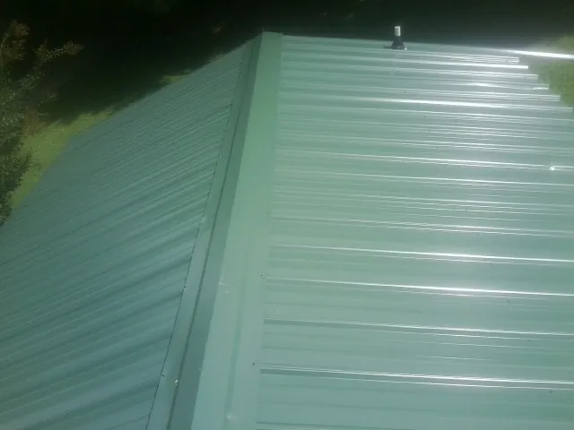 New green metal panels meeting at the ridge of a roof — Flat Roof Repair work by our crew in Cleves