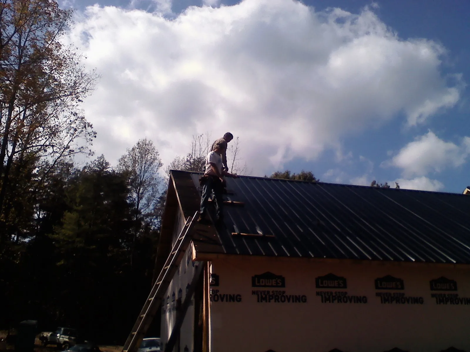 Roofer fastening dark metal panels high against a cloudy sky, from a Roof Inspection job in Cleves
