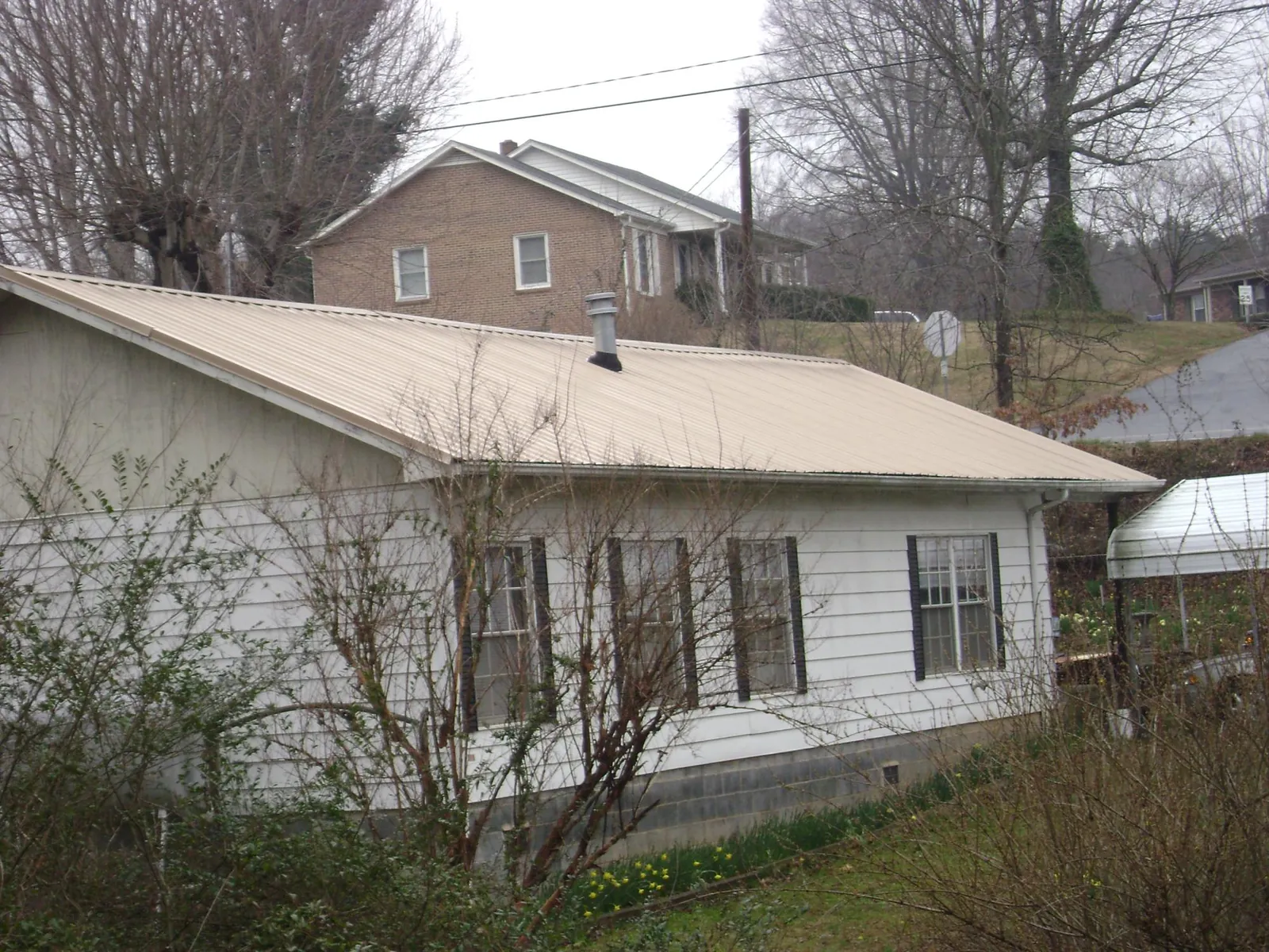 Tan metal roof on a white sided house set into a hillside — Commercial Roofing by Roofing Brothers in Cleves